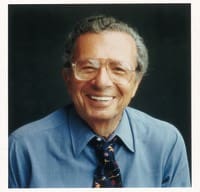 A man in glasses and a tie smiling for the camera.